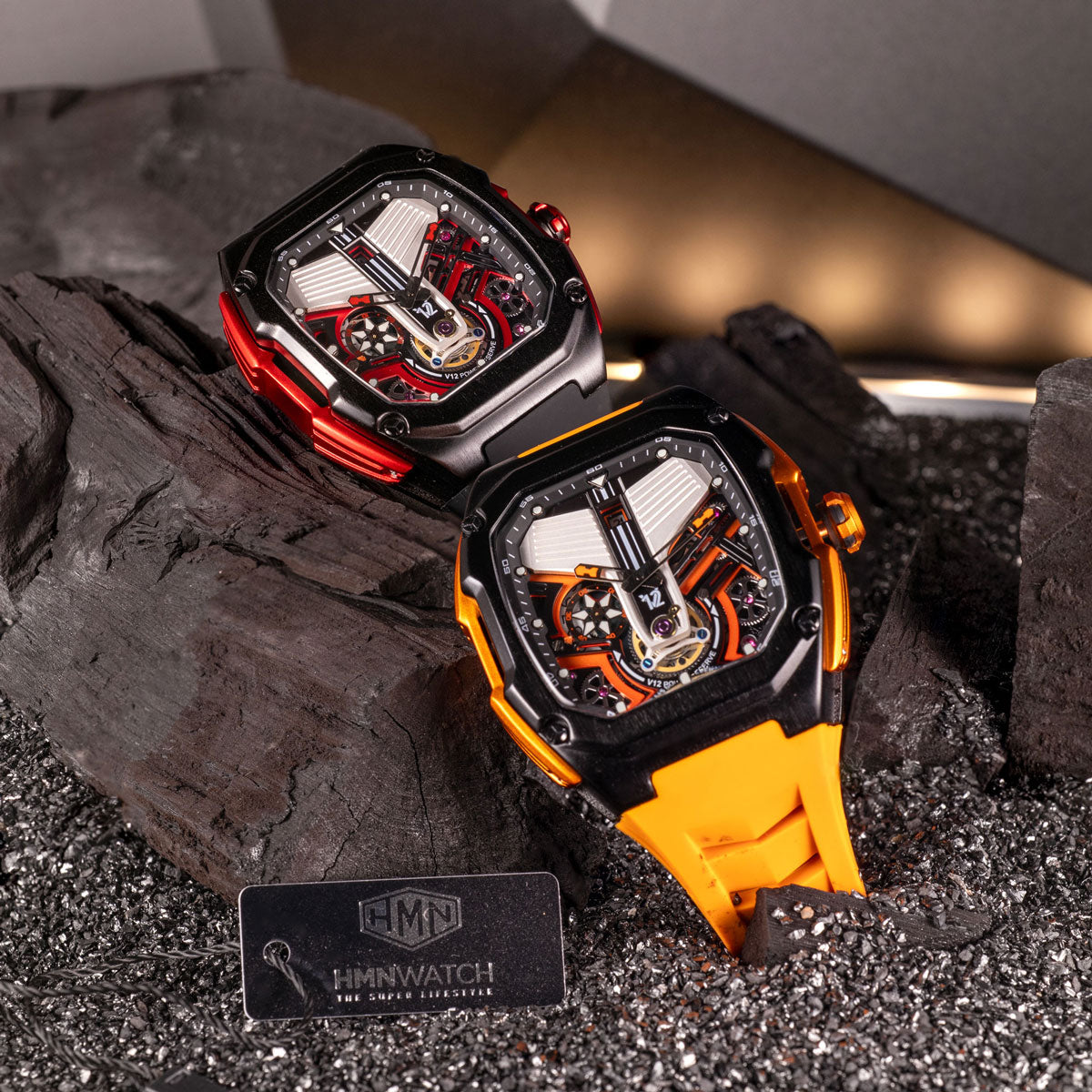 Two V12 Engine HMN watches with open cases on a dark textured surface